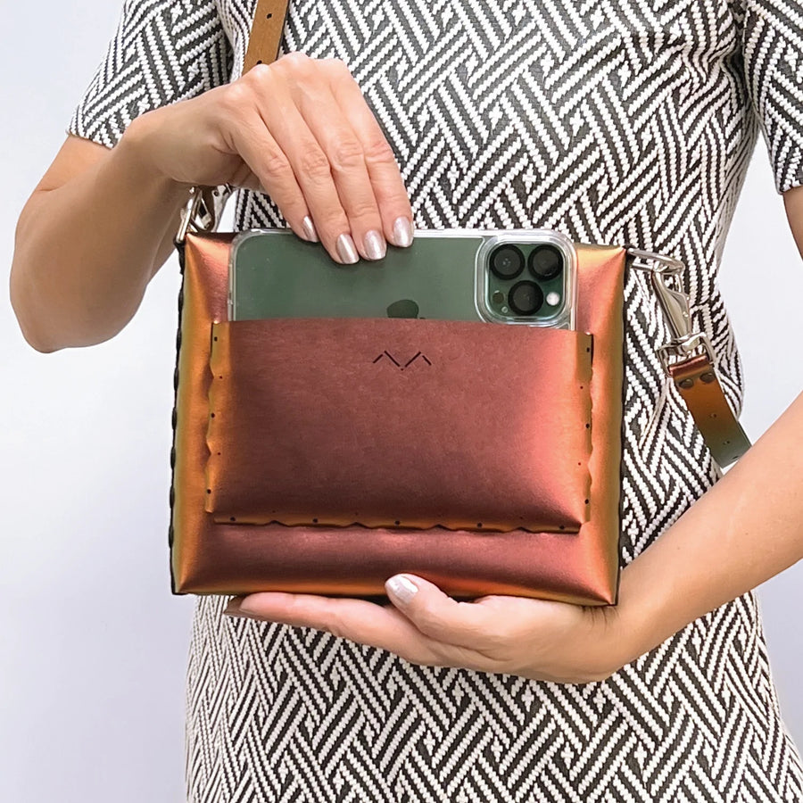 Woman inserting iPhone Max into rear pocket of Ruby Square Bubble Bag. 